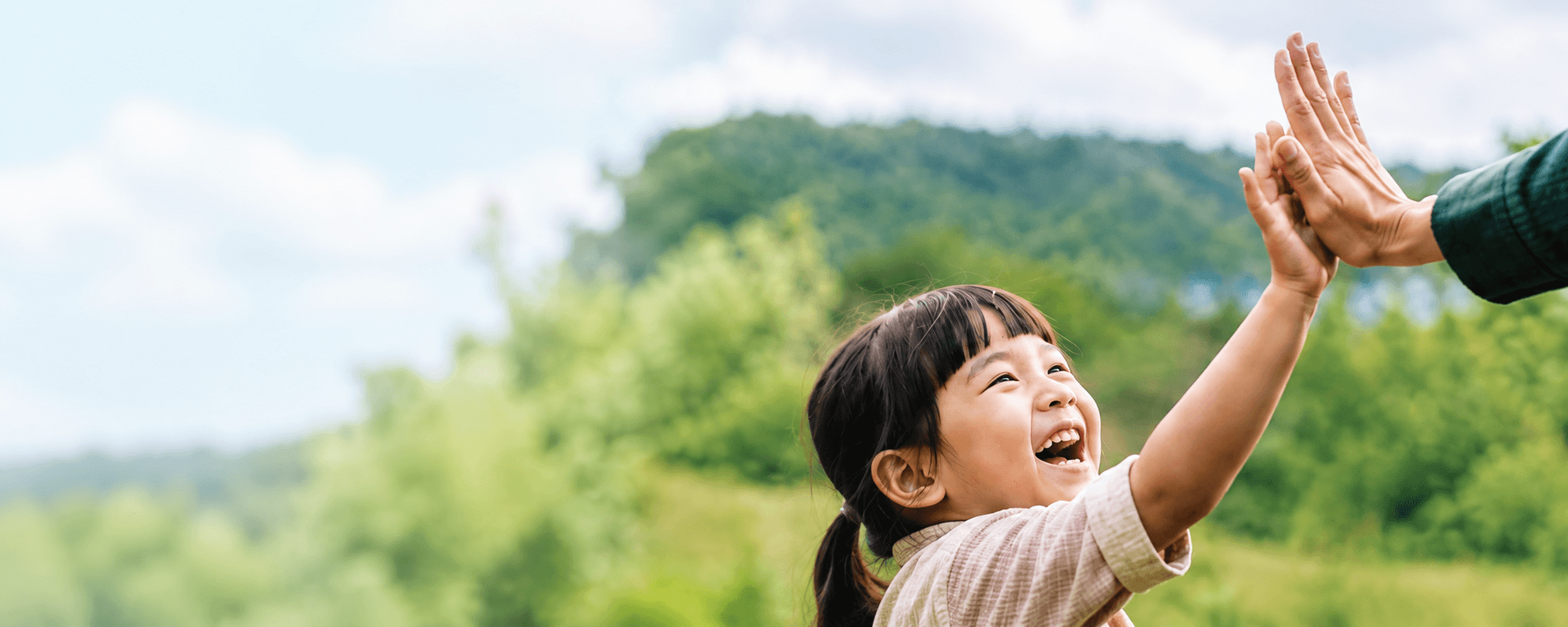 Em nhỏ vui vẻ high-five với người lớn giữa khung cảnh thiên nhiên xanh
